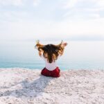 woman sitting on cliff near body of water